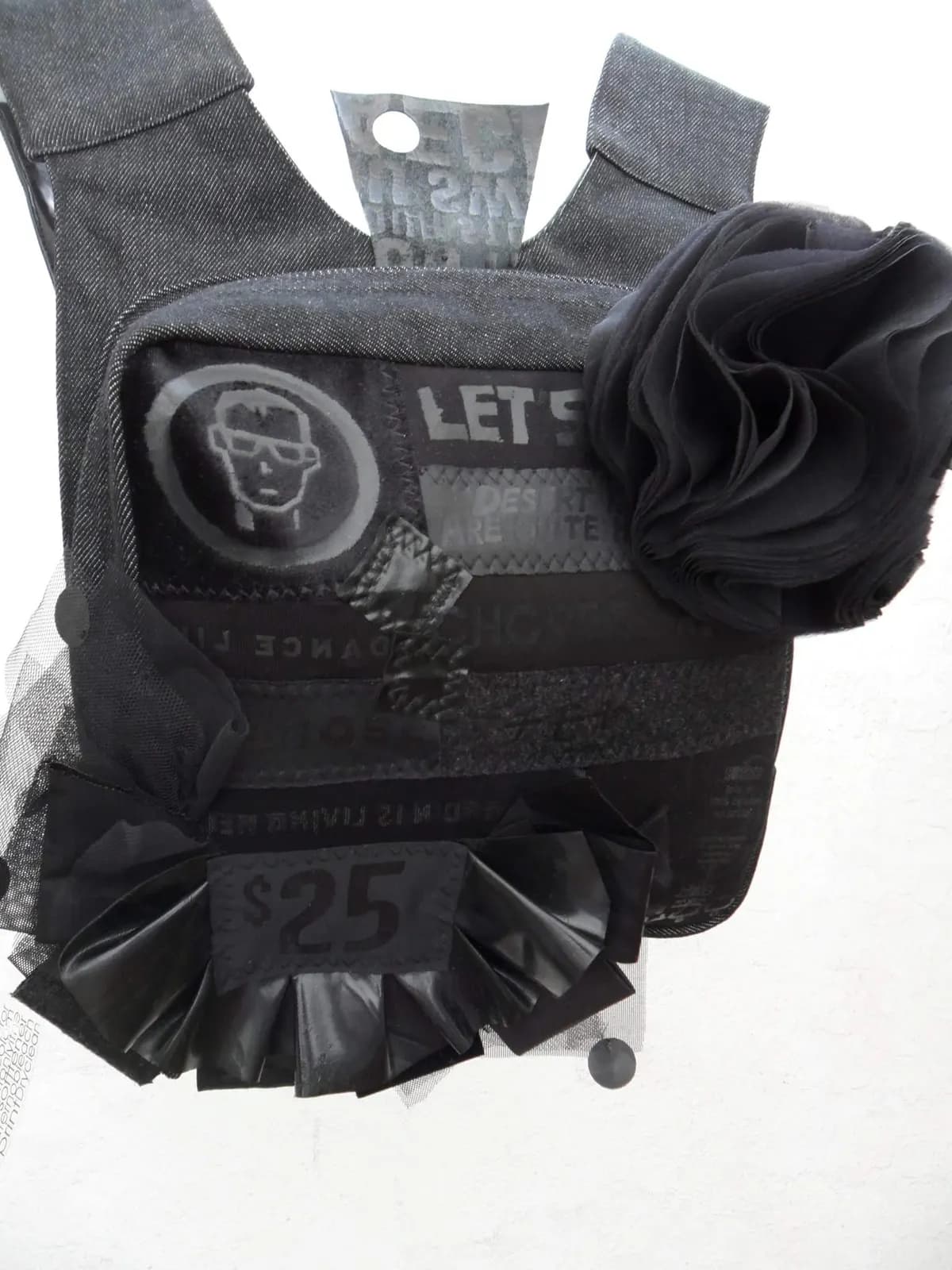 Chaleco-bolso en denim negro intervenido con serigrafía, apliques cosidos, flor de tul y etiqueta estampada.