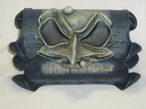 Pieza escultórica en textil endurecido azul con relieve de máscara, firmada por el autor.