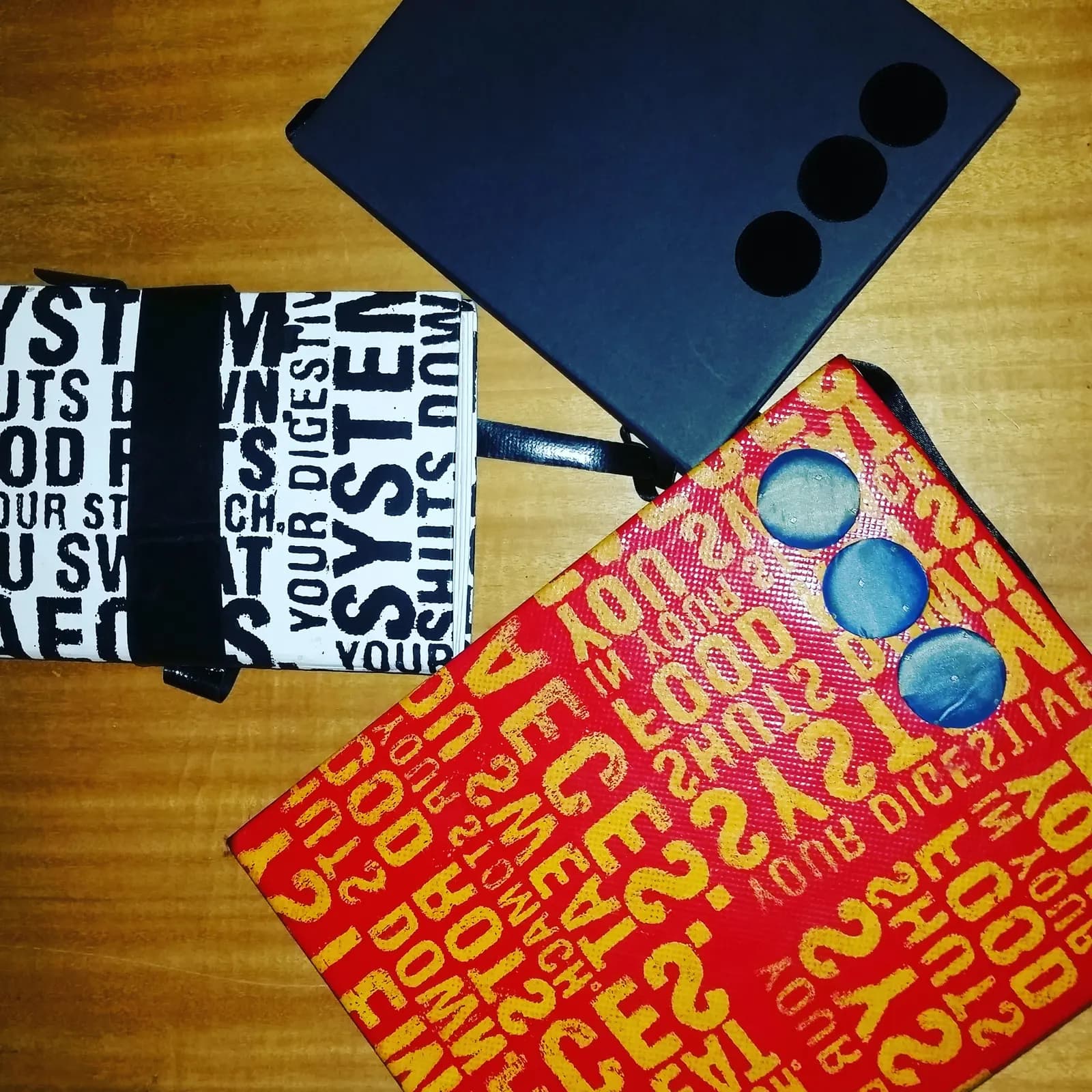 Tres libretas artesanales con cubiertas serigrafiadas tipográficas en blanco y negro, azul, y rojo con amarillo.