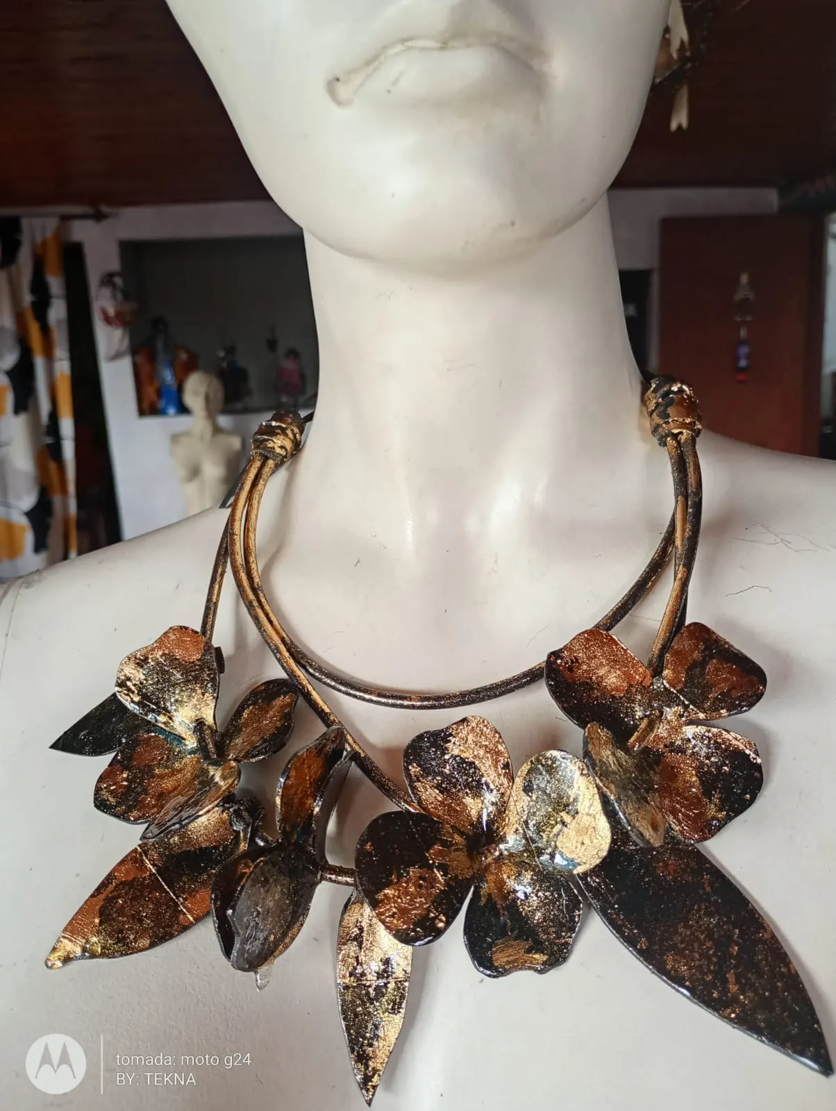 Collar de gran formato con flores y hojas de caucho reciclado acabadas en cobre y oro, exhibido sobre maniquí.