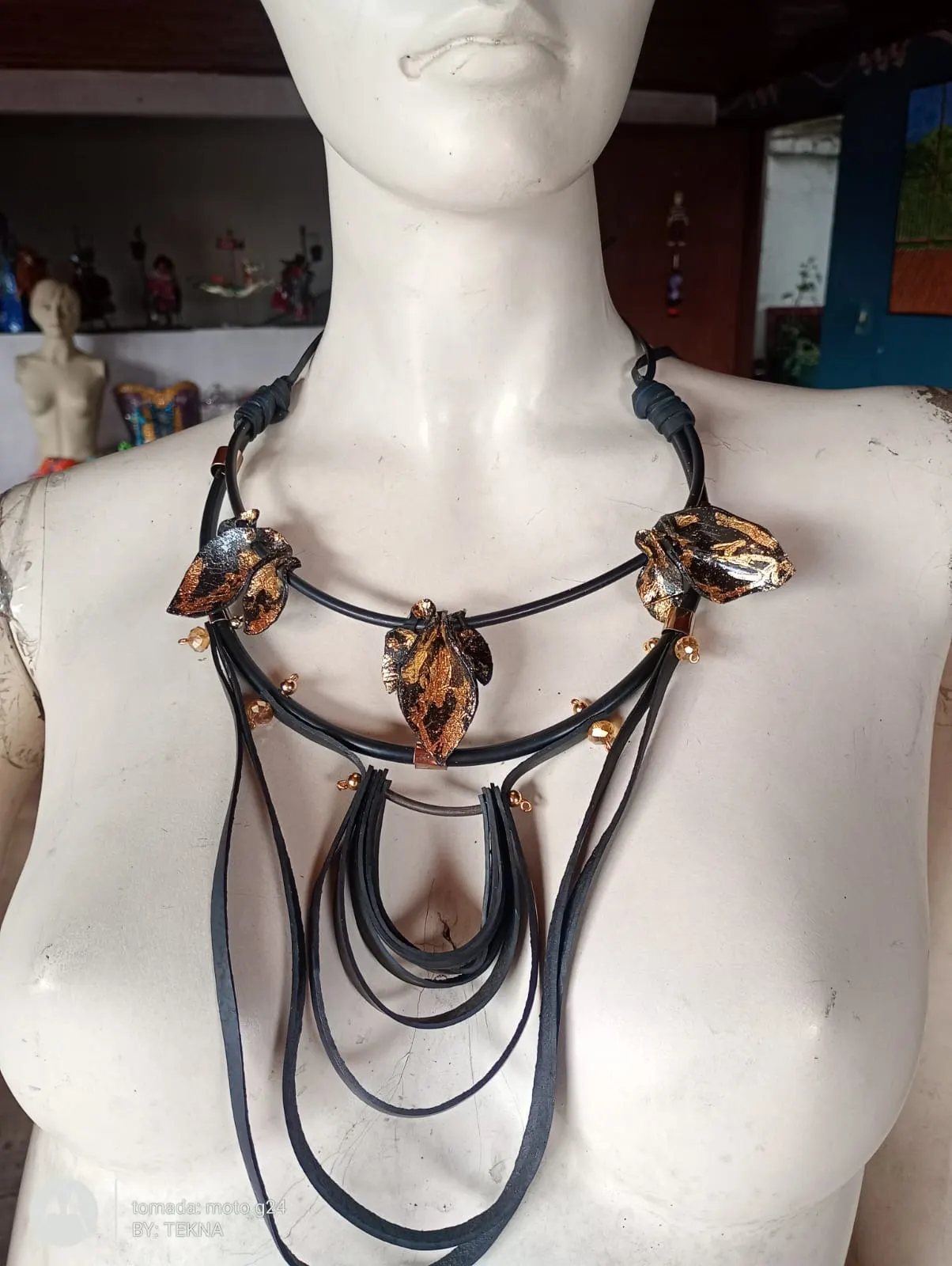 Collar escalonado en caucho negro con hojas doradas y arcos colgantes elaborados con cámara de llanta reutilizada, sobre maniquí.