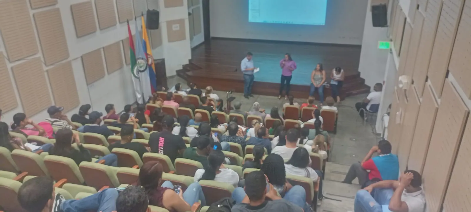 Socialización ante el público en un auditorio con banderas de Colombia y del municipio, con la platea llena de asistentes.