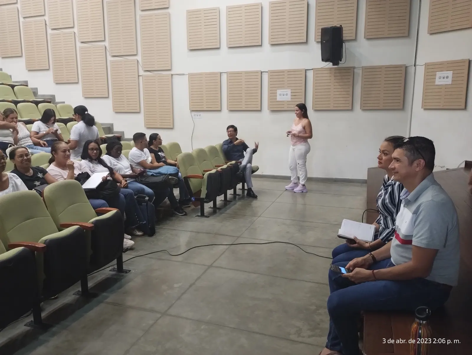 Gestora de pie dirige una sesión de socialización ante asistentes sentados en un auditorio con paneles acústicos.
