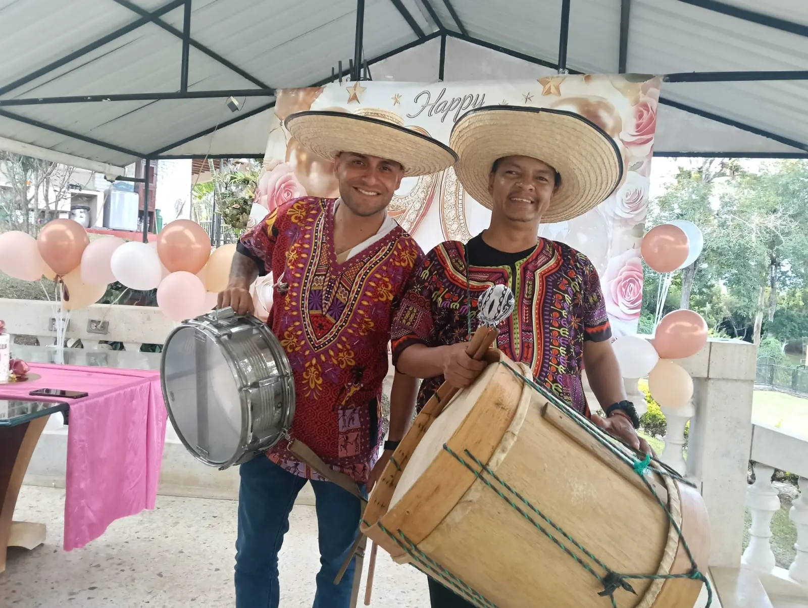Dos músicos con sombreros de paja y camisas tradicionales interpretan redoblante y tambora en una celebración al aire libre.