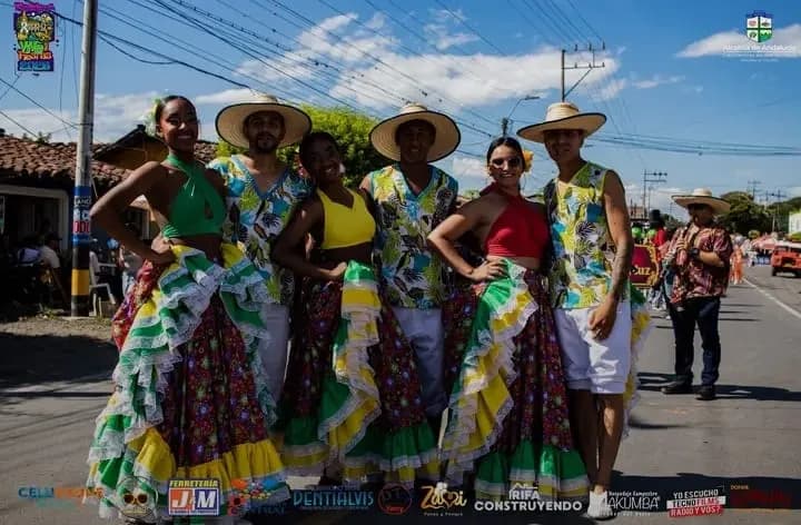 Grupo de danza folclórica con faldas de colores y sombreros de paja desfila por la vía principal durante las fiestas del municipio.