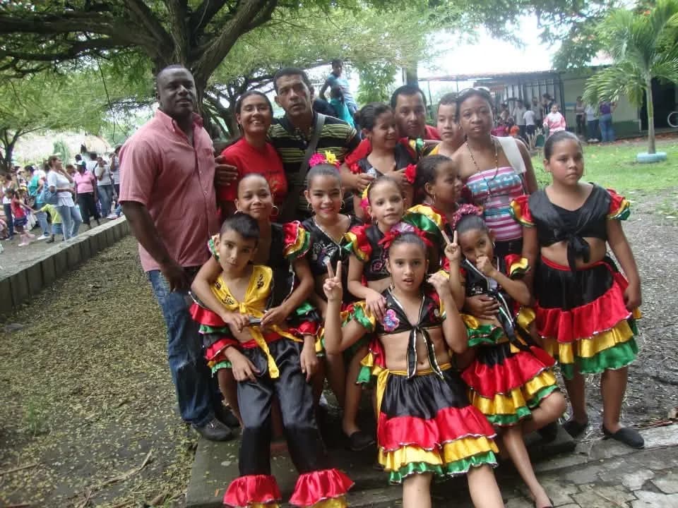 Niñas y niños con vestuario folclórico de colores junto a sus familias y formadores en un espacio al aire libre tras una presentación.