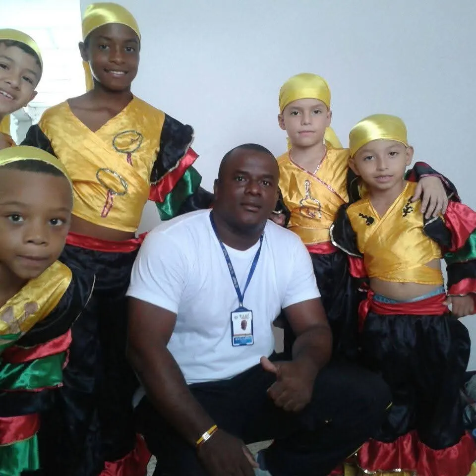 Jesús Albeiro Angulo junto a un grupo de niños con vestuario folclórico en amarillo, negro, rojo y verde, antes de una presentación de danza.