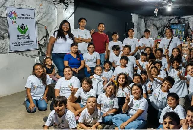 Fotografía grupal de la actividad comunitaria Mochila Atrapasueños, con niños y acompañantes reunidos en un salón comunal