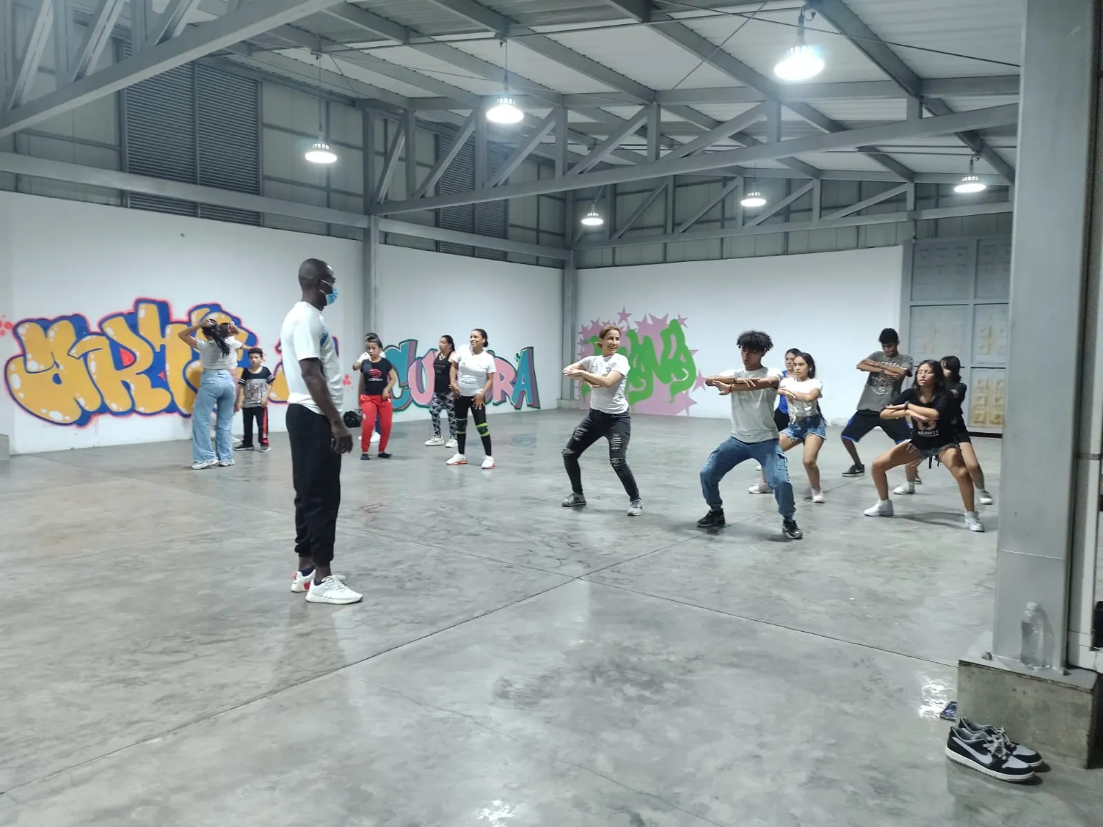 Orlando dirige un ensayo de danza urbana con un grupo de jóvenes en una bodega cultural con grafitis de arte y cultura en las paredes.
