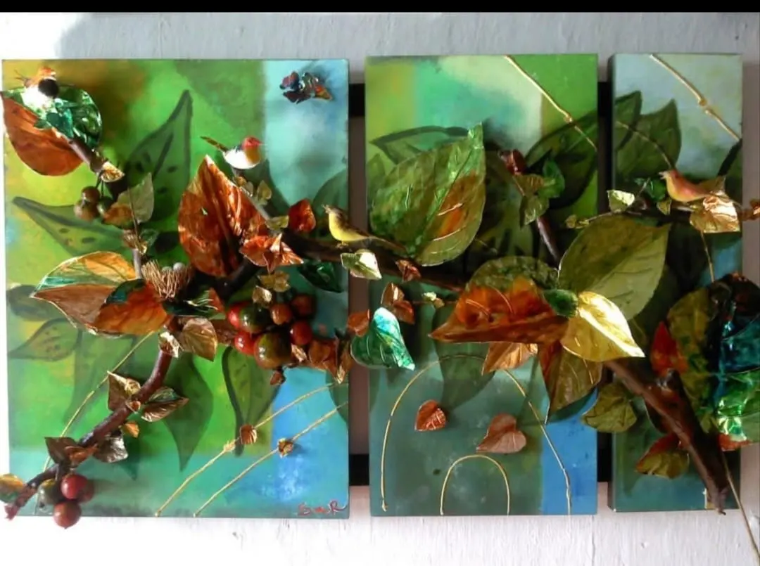 Tríptico en técnica mixta con ramas, hojas metalizadas, frutos y pequeñas aves en relieve sobre fondos verdes y azules.