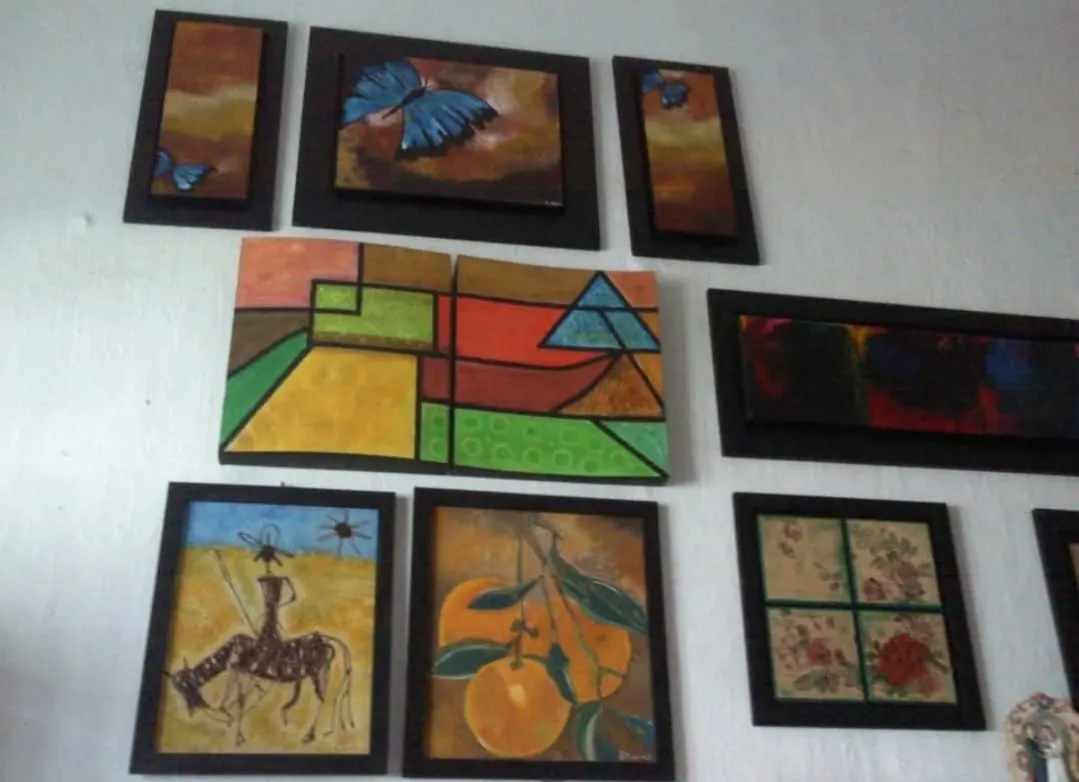 Muro con obras enmarcadas: mariposas azules, composición geométrica, Don Quijote a caballo y bodegón de naranjas.