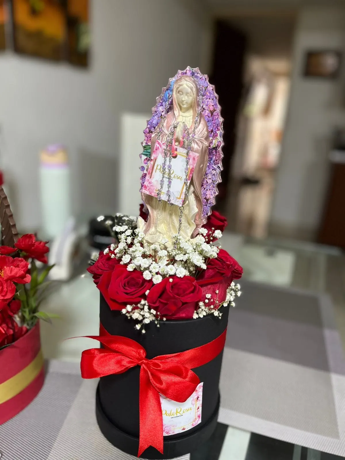 Caja floral negra con rosas rojas y lazo, coronada por una Virgen de Guadalupe decorada en tonos rosa y lila, pieza de Palo Rosa Decoración.